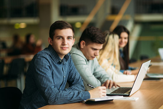A college-age young man working on his laptop in the school library